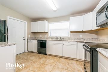 Cocoa house for rent - A kitchen with white cabinets and a black fridge.