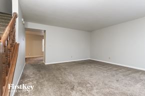 Indianapolis house for rent - A spacious empty room with a carpeted floor and a staircase on the left side.