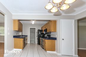 Port St. Lucie house for rent - a kitchen with wooden cabinets and black appliances and a hallway with a door