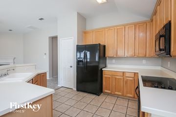 Rockwall house for rent - a kitchen with wooden cabinets and a black refrigerator