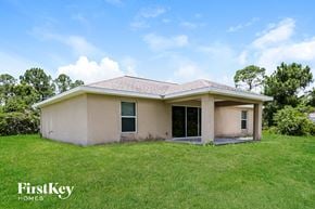 Lehigh Acres house for rent - A house with a brown roof and a white wall is surrounded by green grass.