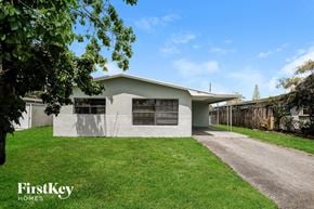 Hollywood house for rent - A house with a white exterior and a grey roof is surrounded by a green lawn.