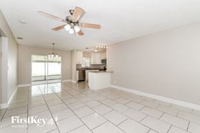 Fort Myers house for rent - A spacious room with a fan and a kitchen in the background.