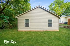 Kannapolis house for rent - A small house with a brown roof and a beige siding is surrounded by green grass and trees.