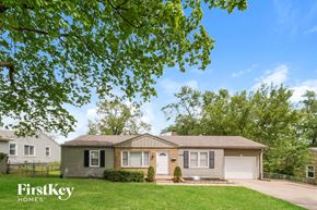 Raytown house for rent - A house with a brown roof and a white garage door is surrounded by greenery.
