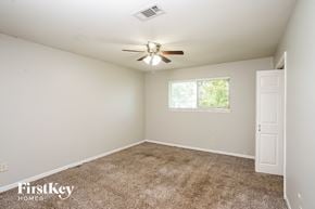 La Porte house for rent - A room with a carpeted floor, a ceiling fan, and a window with a view of trees outside.