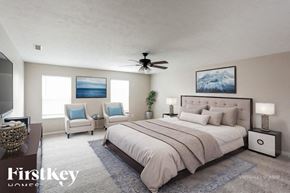 Noblesville house for rent - A bedroom with a large bed, a ceiling fan, and two chairs.