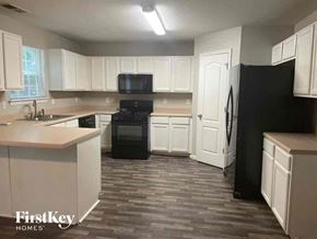 Hampton house for rent - an empty kitchen with white cabinets and black appliances