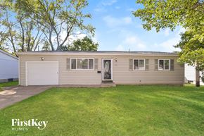 Florissant house for rent - A small house with a garage door is surrounded by a grassy lawn.