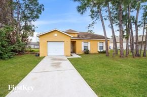 Sebastian house for rent - A yellow house with a white garage door is surrounded by greenery.