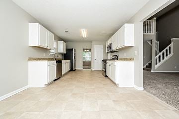 Hampton house for rent - a kitchen with white cabinets and a hallway with stairs