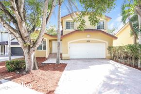Miami house for rent - A yellow house with a white garage door and a tree in front.