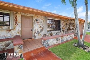 Sunrise house for rent - a house with a pink door and a porch with a palm tree