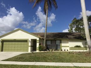 Wellington house for rent - A house with a green garage door and a palm tree in front.