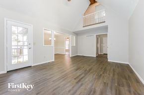 Olathe house for rent - A spacious room with wooden floors and white walls, with a balcony on the upper floor.