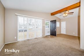Florissant house for rent - A spacious living room with a ceiling fan and a view of a fence and trees outside the window.