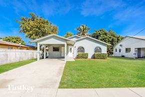 Dania Beach house for rent - A white house with a brown roof is surrounded by a green lawn.