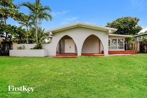 Miami house for rent - a small white house with an arched porch and a green lawn