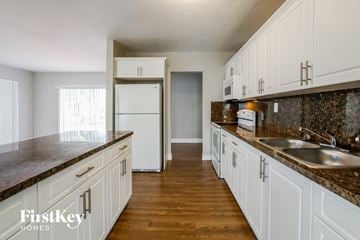 Miami house for rent - a kitchen with white cabinets and granite counter tops and a sink