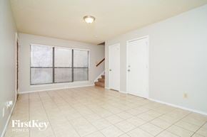 Lewisville house for rent - A spacious room with a window covered by blinds, a staircase, and a door.