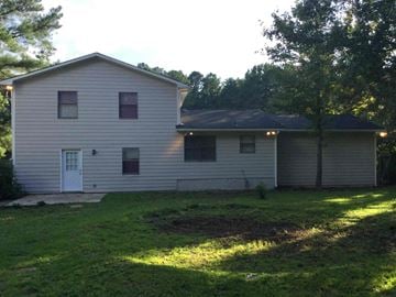 Jonesboro house for rent - A house with a white door and windows is surrounded by trees.