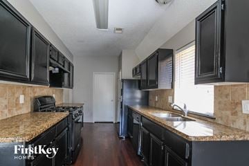 Houston house for rent - a kitchen with black cabinets and granite counter tops and a sink