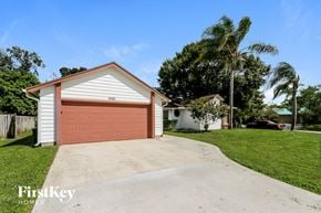 Port St. Lucie house for rent - a pink garage door on a white house with a driveway