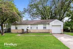 Gladstone house for rent - A white house with a brown roof and a garage door is surrounded by green grass and trees.