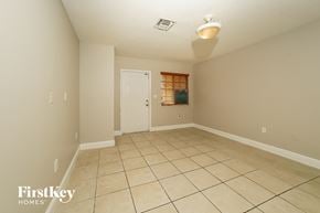 Homestead house for rent - A spacious room with beige walls and tile flooring, featuring a door and a window with blinds.