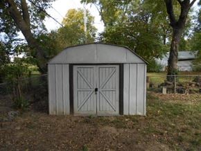 Florissant house for rent - A white shed with a grey roof is surrounded by trees.
