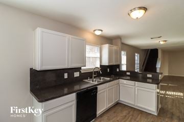 Houston house for rent - a kitchen with white cabinets and black counter tops and a sink