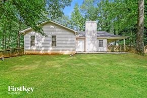 Conyers house for rent - A house with a white exterior and a chimney is surrounded by a grassy lawn and trees.