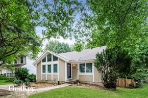 Kansas City house for rent - A house with a white exterior and a brown roof is surrounded by greenery.