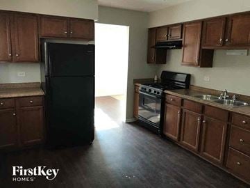 Dolton house for rent - an empty kitchen with dark wood cabinets and a black refrigerator