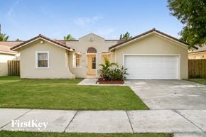 Miami house for rent - a beige house with a white garage door and a lawn