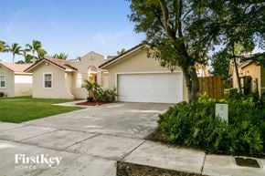 Miami house for rent - a beige house with a white garage door and a tree