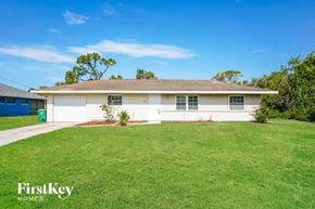 Port Charlotte house for rent - A white house with a brown roof and a green trash can in front of it.