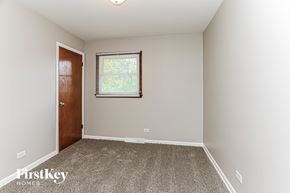 South Holland house for rent - A room with a carpeted floor, a window with a view of trees, and a wooden door.