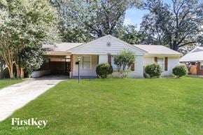 Memphis house for rent - A white house with a garage is surrounded by green grass and trees.
