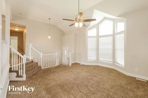 Raymore house for rent - A spacious room with a carpeted floor, a ceiling fan, and a staircase with white railings.