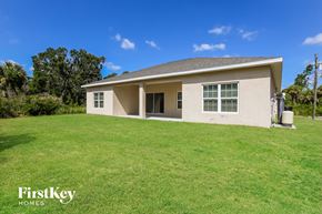 North Port house for rent - a beige house with a grassy yard and trees in the background