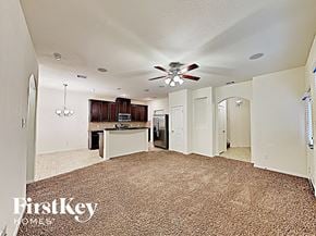 Houston house for rent - A carpeted room with a ceiling fan and a kitchen area in the background.