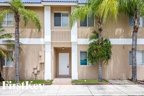 Miami house for rent - A beige two-story apartment building with a balcony and palm trees in front.