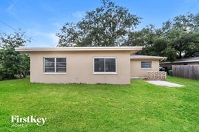 Clearwater house for rent - a small tan house with a grassy yard and a tree