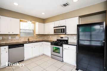 Cypress house for rent - A kitchen with white cabinets and a black fridge.