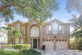 Katy house for rent - A brick house with a black door and windows is surrounded by trees.