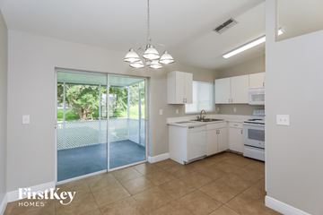 Cape Coral house for rent - A kitchen with white cabinets and appliances, a tiled floor, and a sliding glass door leading to a patio.