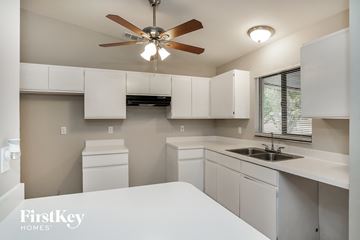 Cape Coral house for rent - a kitchen with white counters and white cabinets and a ceiling fan