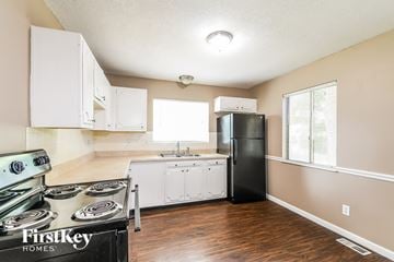 Florissant house for rent - A kitchen with a black refrigerator, white cabinets, and a stove top oven.
