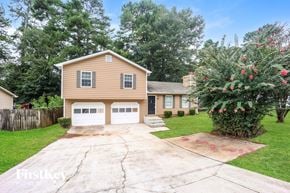 Lithonia house for rent - A house with a brown siding and a white garage door is surrounded by a fence and a tree with red flowers.